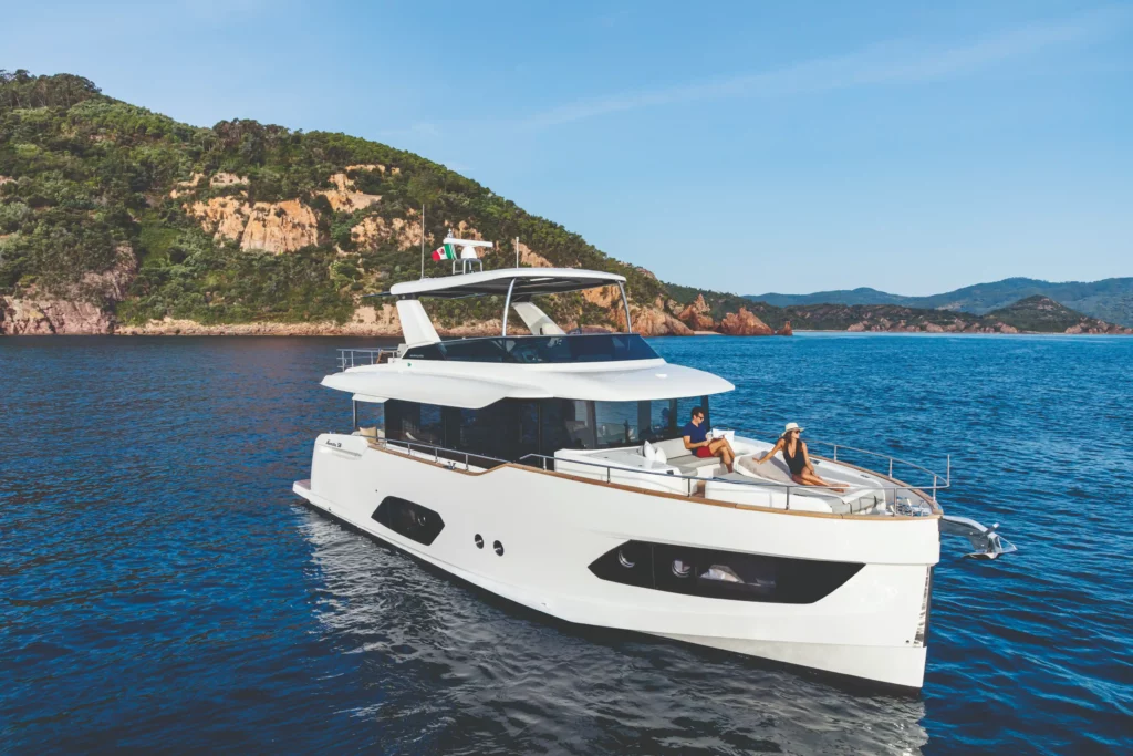 Luxe jacht Absolute Navetta 58 vaart langs een rotsachtige kustlijn met ontspannen passagiers aan boord.