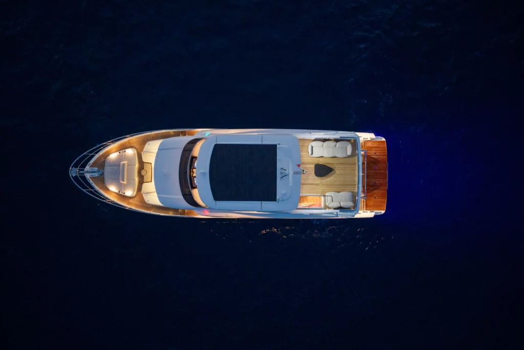 Luchtfoto van de luxejacht Absolute Navetta 66 op een rustig donkerblauw water, verlicht met sfeervolle verlichting.