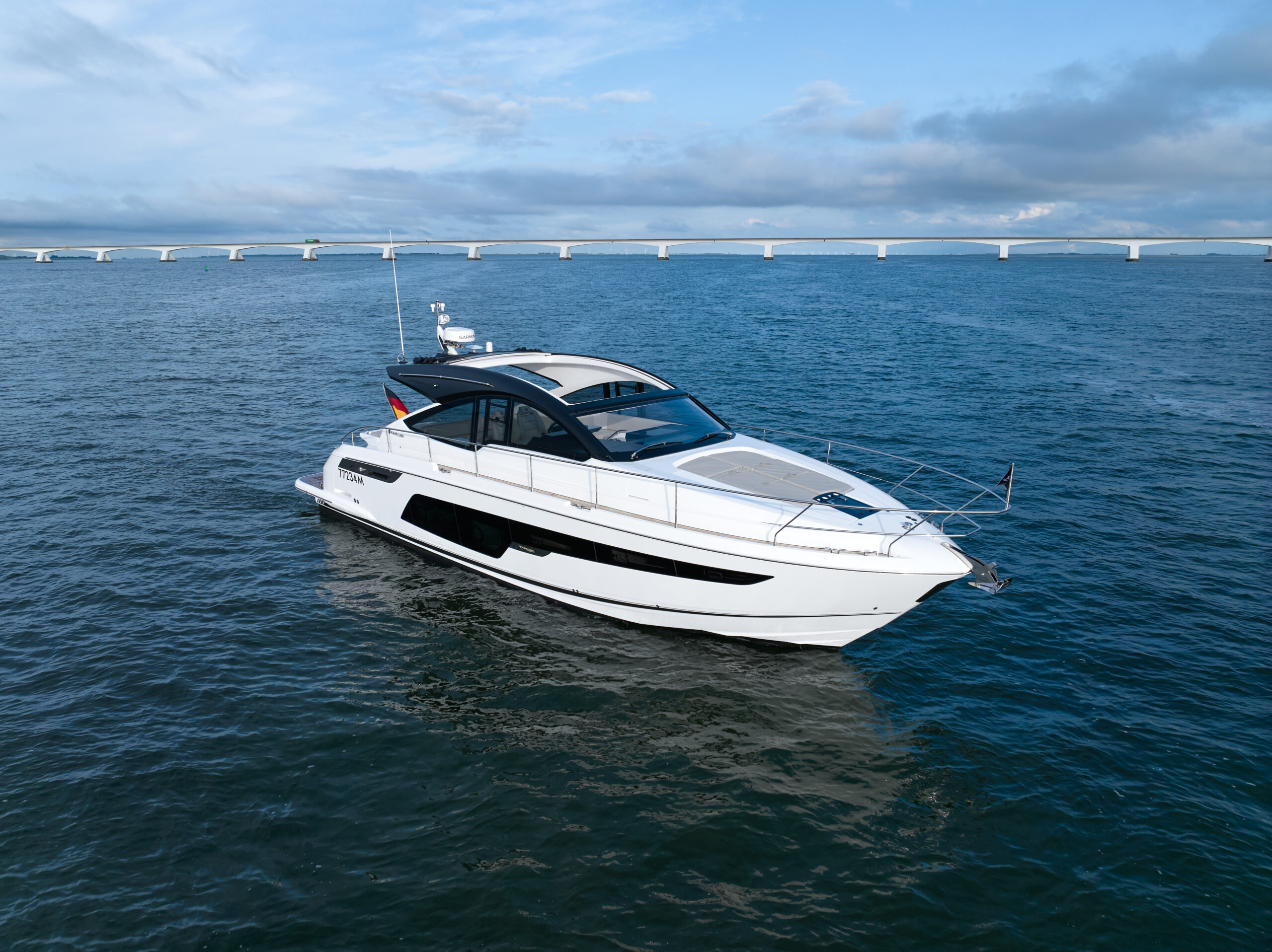 Luxe motorjacht genaamd "Titan" vaart op open water met een lange brug op de achtergrond.