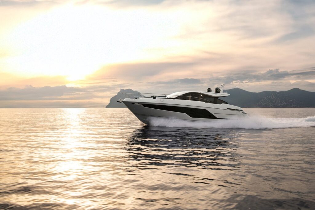 Een luxe Fairline Targa 58 GTO vaart bij zonsondergang over een kalme zee, met bergen op de achtergrond.