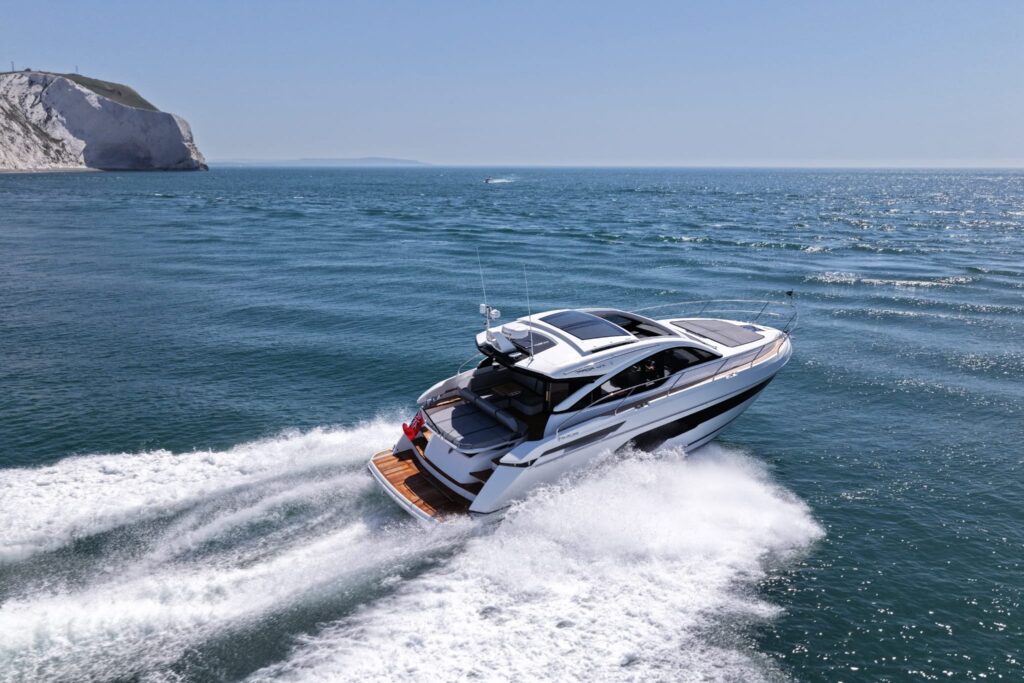 Een luxe Targa 47 GT jacht vaart op volle snelheid nabij een rotsachtige kustlijn met helderblauw zeezicht.